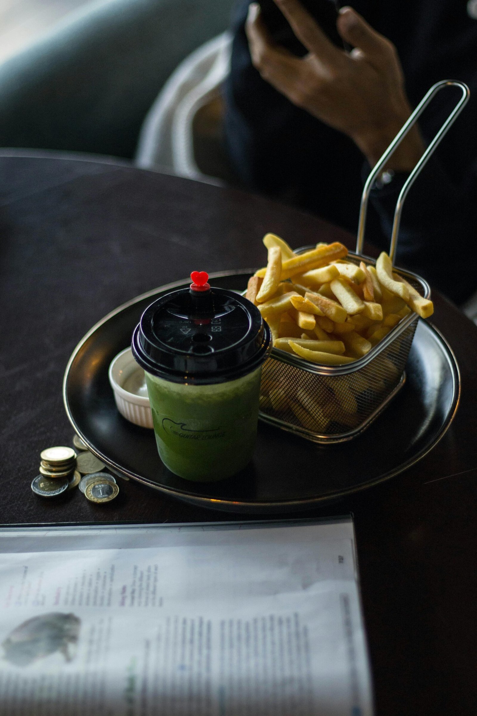 A plate with french fries and a green drink on a table at a cafe.